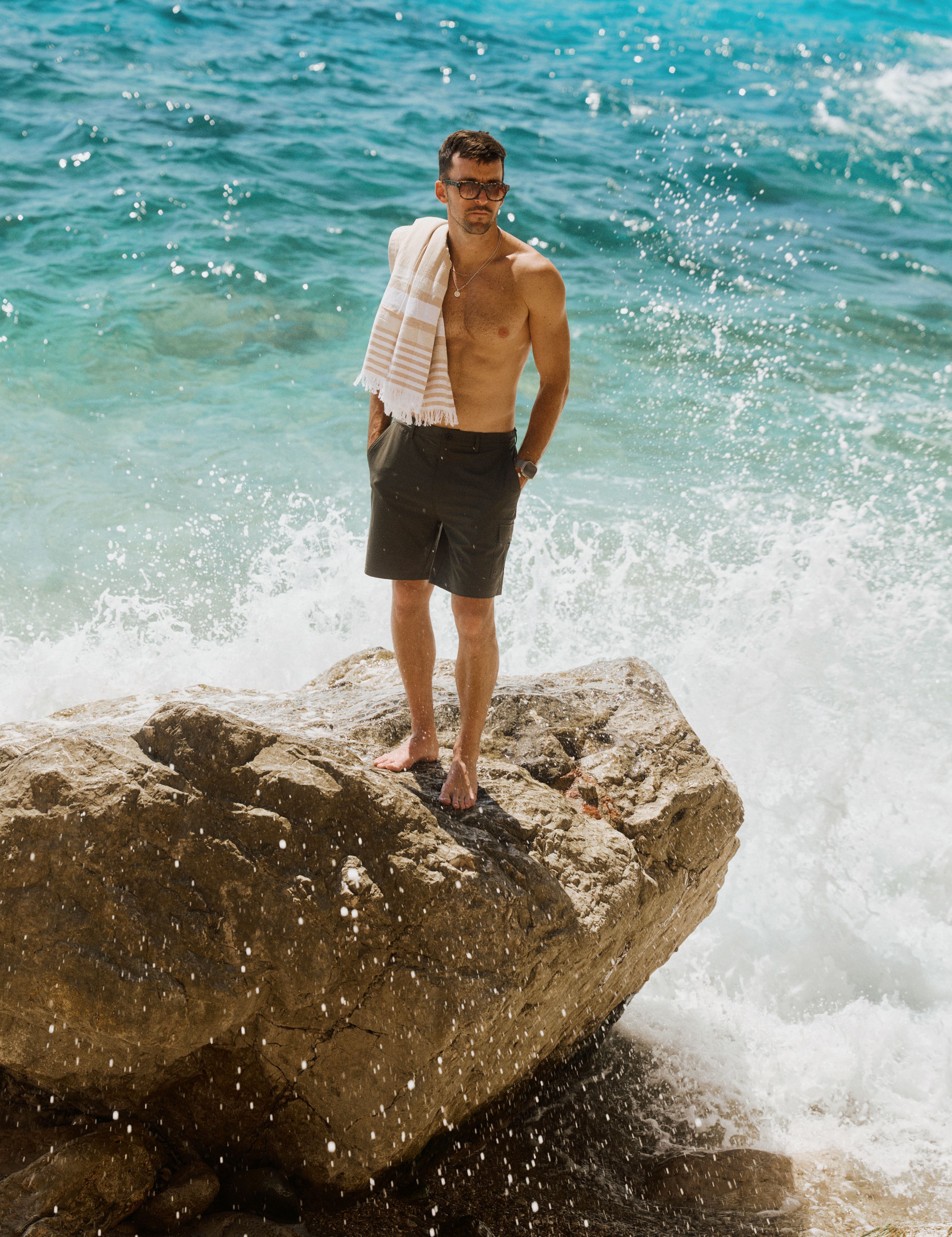 The Board Shorts in khaki — worn while standing on a rock with crashing waves