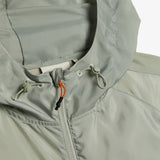 A close-up shot of the hood and neckline of The Running Jacket in Sage Green, highlighting the drawstring toggles and the contrast orange and black zipper puller. | c'est normal