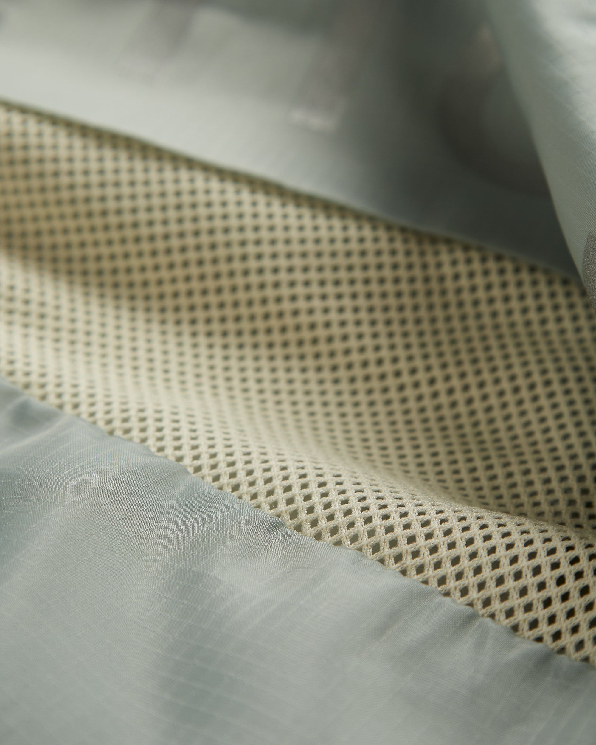 A detailed close-up of The Running Jacket in Sage Green, focusing on the interior mesh lining and back ventilation panel designed to dump heat.