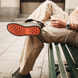 The Sneakers 2.0 in khaki — showing the orange rubber grid sole while sitting on a bench