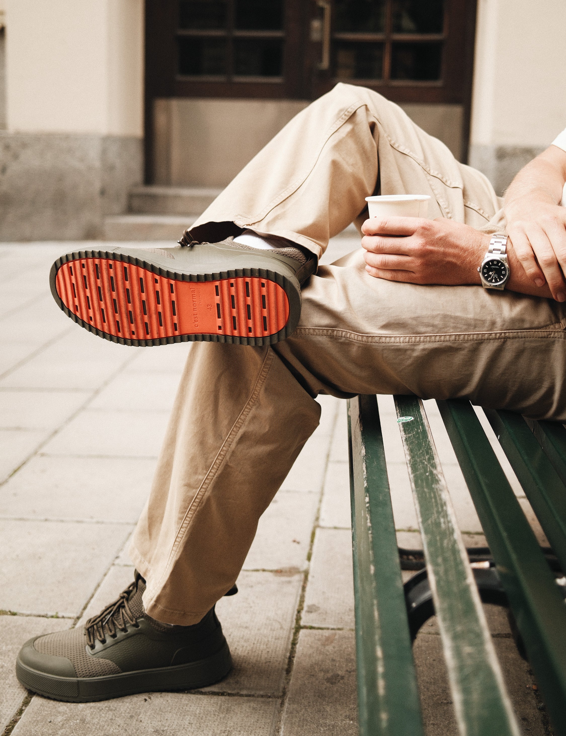 The Sneakers 2.0 in khaki — showing the orange rubber grid sole while sitting on a bench