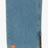 A close-up of the ankle hem of blue jeans, highlighting a metal side zipper and a small orange c'est normal tag.