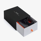 The Sneakers 2.0 in black, presented in a black and grey c'est normal shoebox with an orange pull tab on a white background.