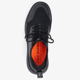 A top-down view of The Sneakers 2.0 in black, laid flat on a white background. The image highlights the tone on tone mesh upper, black laces, and the original orange insole featuring the c'est normal logo.