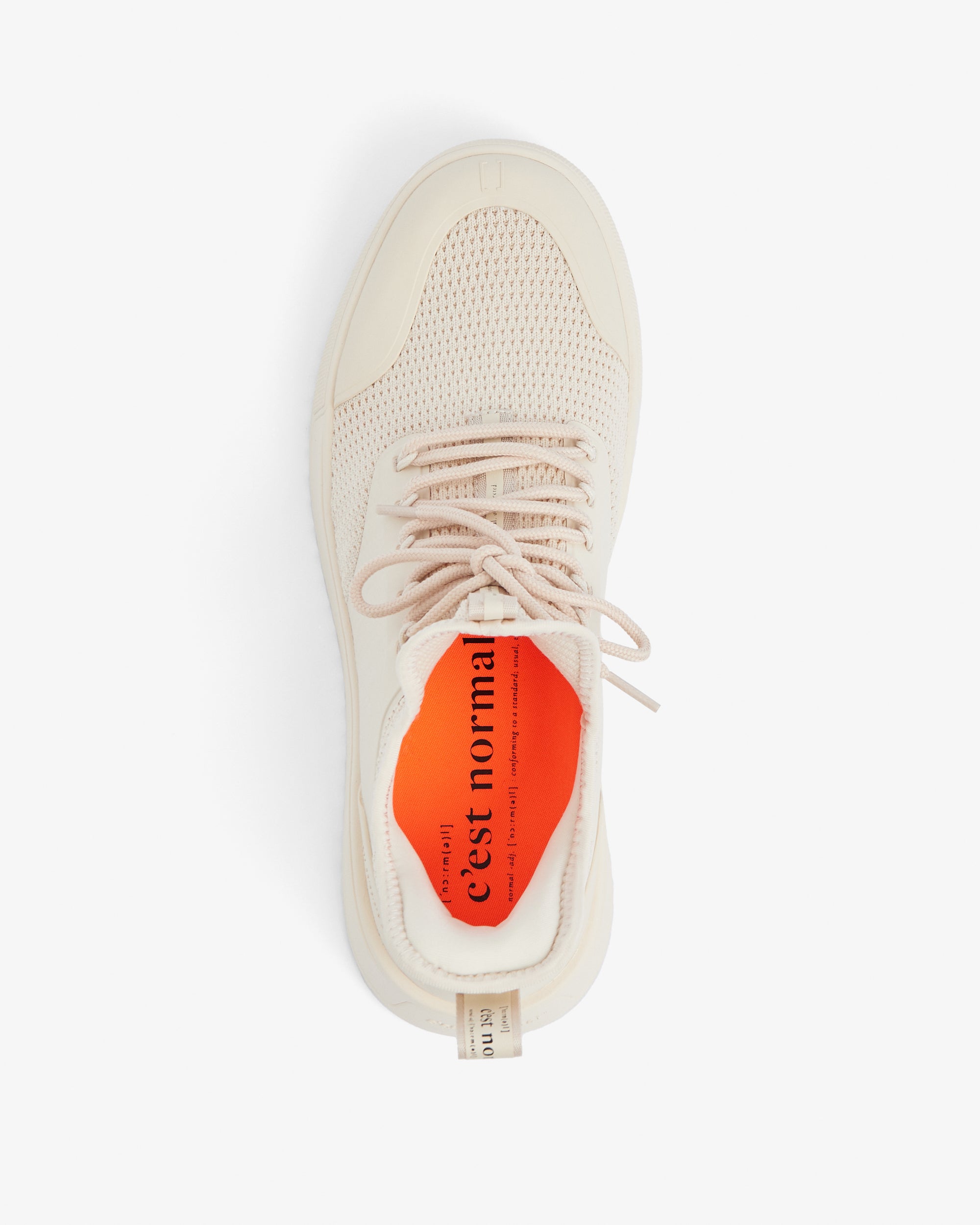 A top-down view of The Sneaker 2.0 in Cream, laid out on a white background. The image highlights the tone-on-tone mesh upper, laces, and the bright orange insole featuring the black c'est normal logo and text.