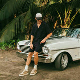 The Linen Resort Shirt in black — worn while leaning on a vintage white car with palm trees
