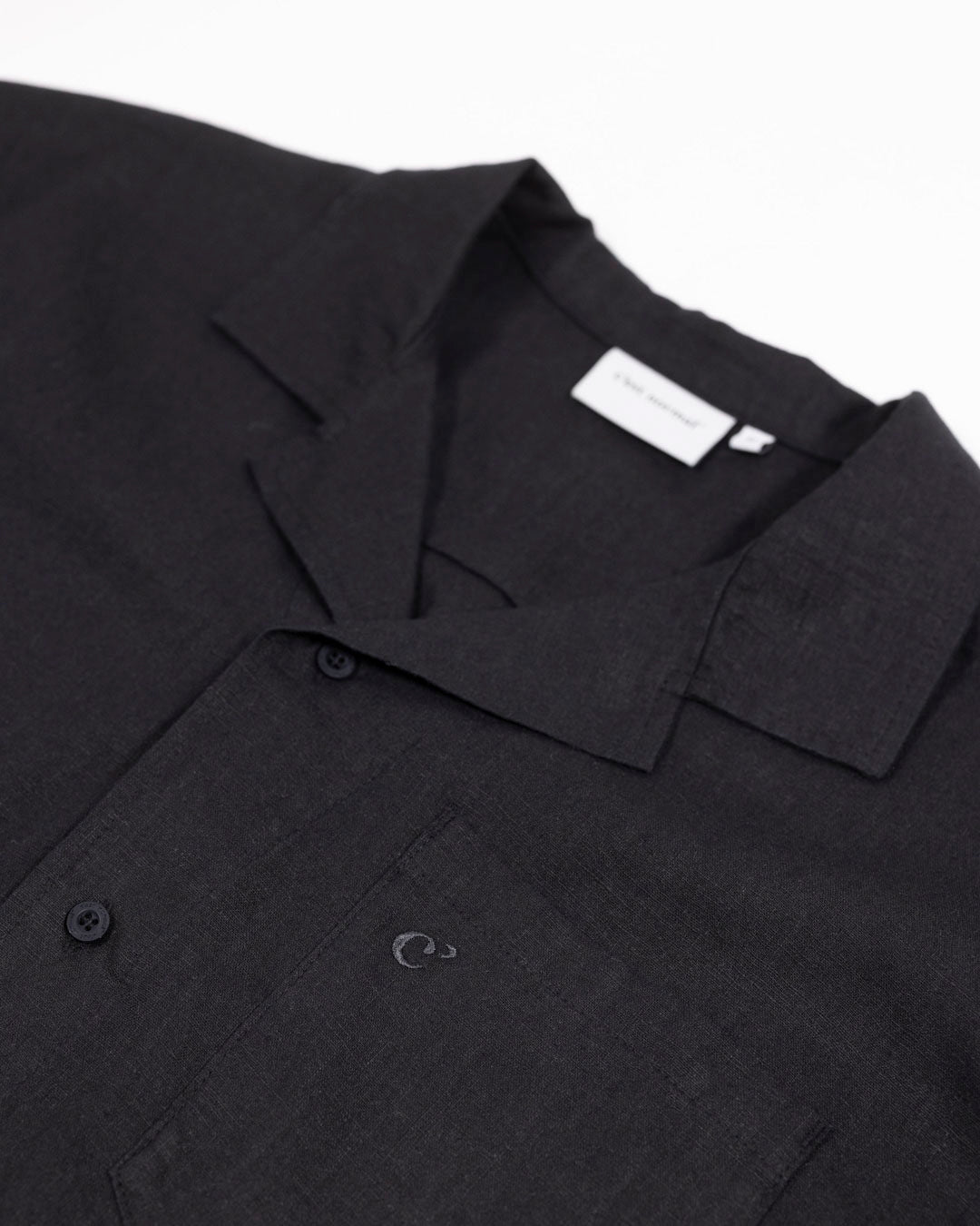 The Linen Resort Shirt in black — close-up of the camp collar and embroidered C' logo