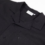 The Linen Resort Shirt in black — close-up of the camp collar and embroidered C' logo