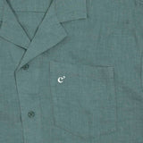 The Linen Resort Shirt in sage — close-up of the chest pocket with an embroidered white logo