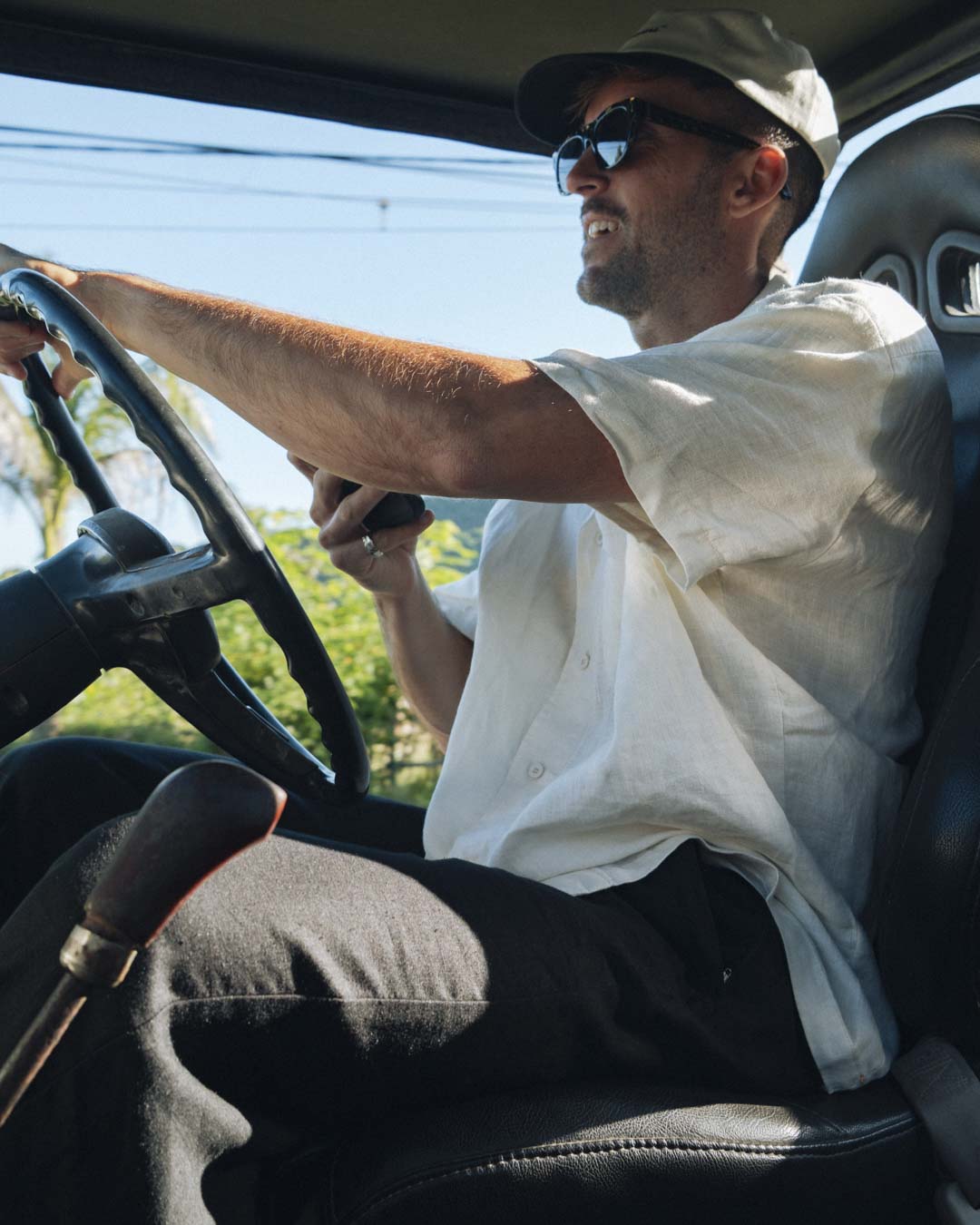 The Tampah Hills Linen Resort Shirt in cream — worn while driving an off-road vehicle