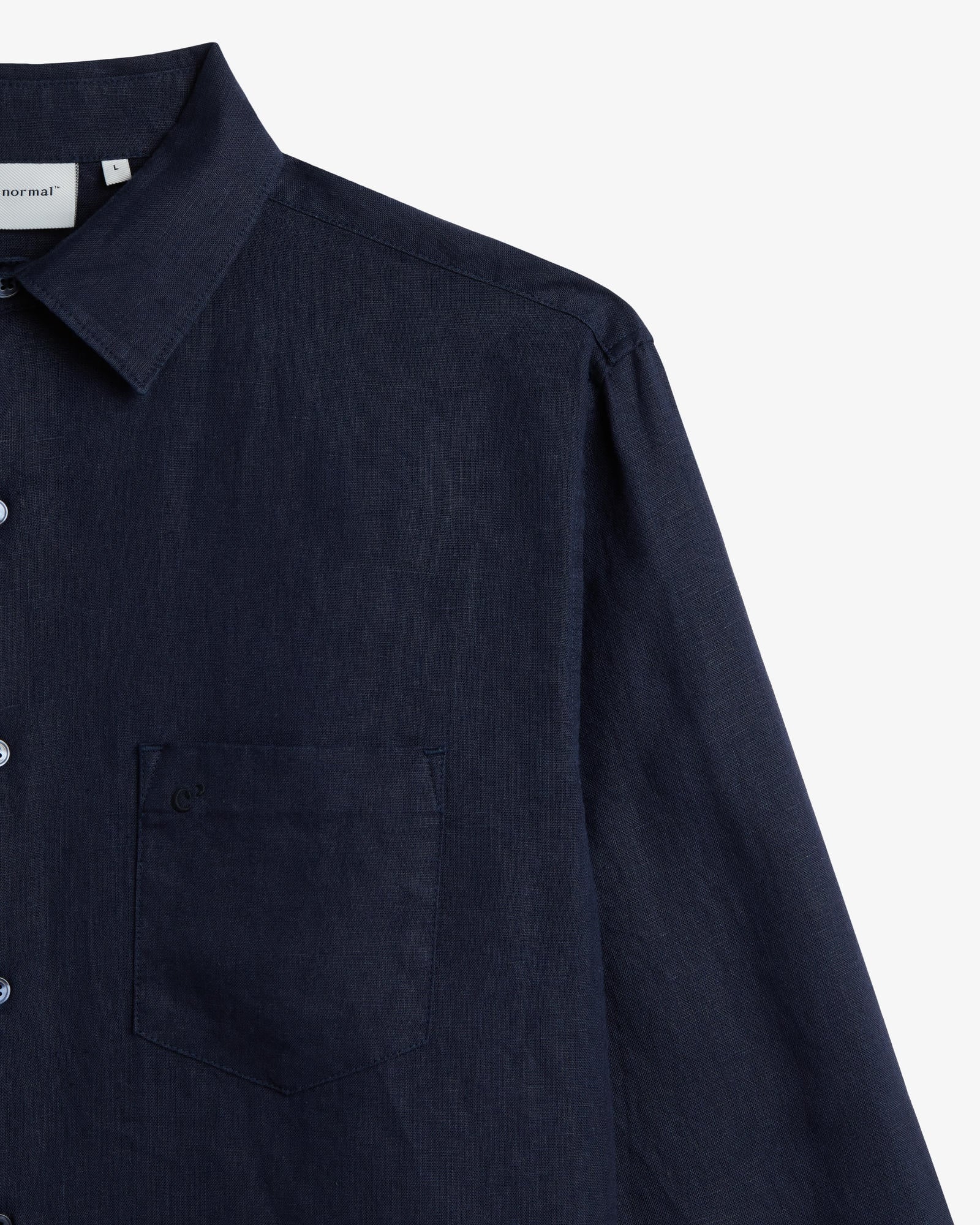 The Daily Linen Shirt in navy — close-up of the chest pocket with tonal embroidery