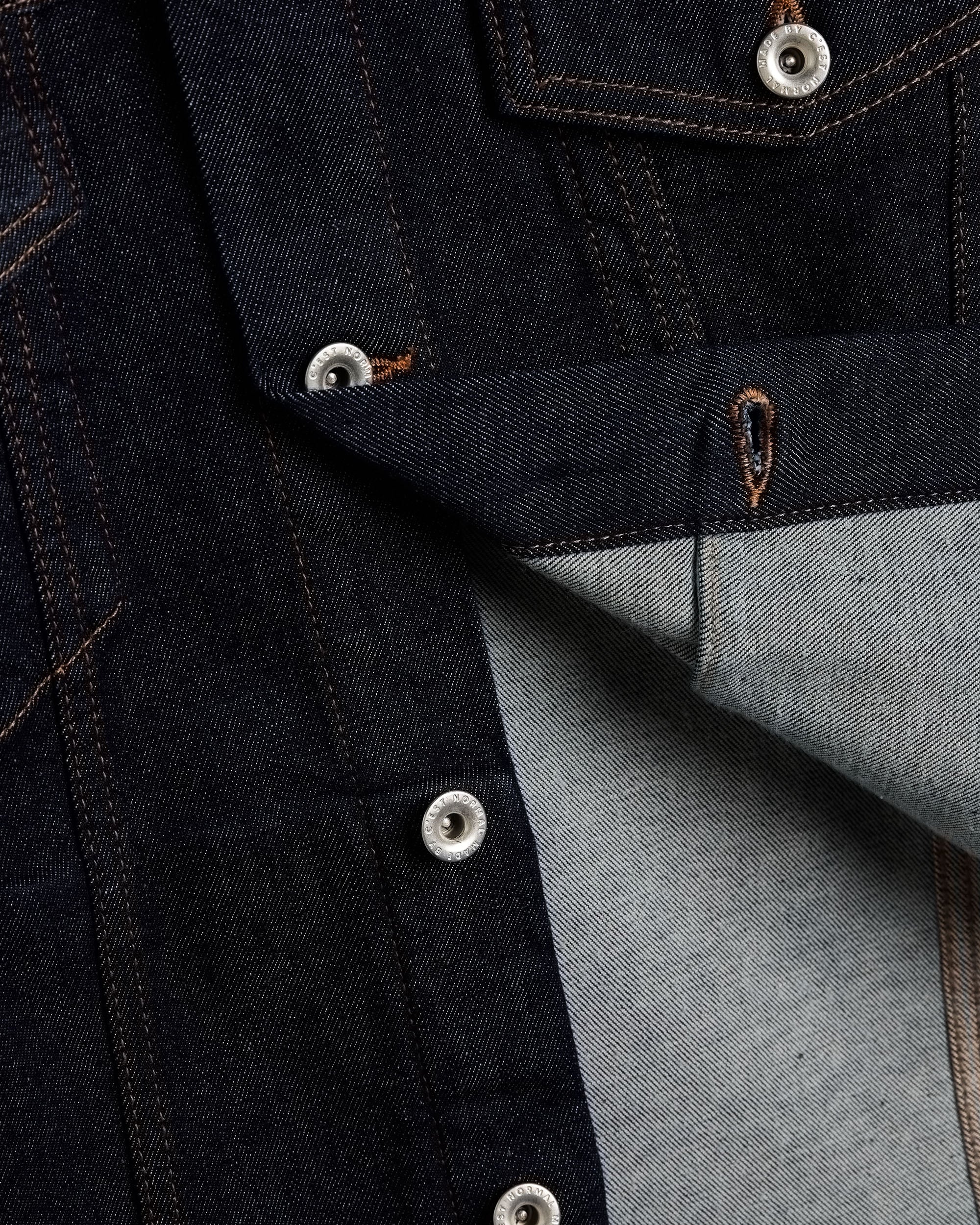 The Denim Jacket in rinse blue — close-up of silver shank buttons engraved with C'est normal