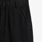 The Holiday Linen Trouser in black — close-up of the waistband and tonal C'est normal embroidery