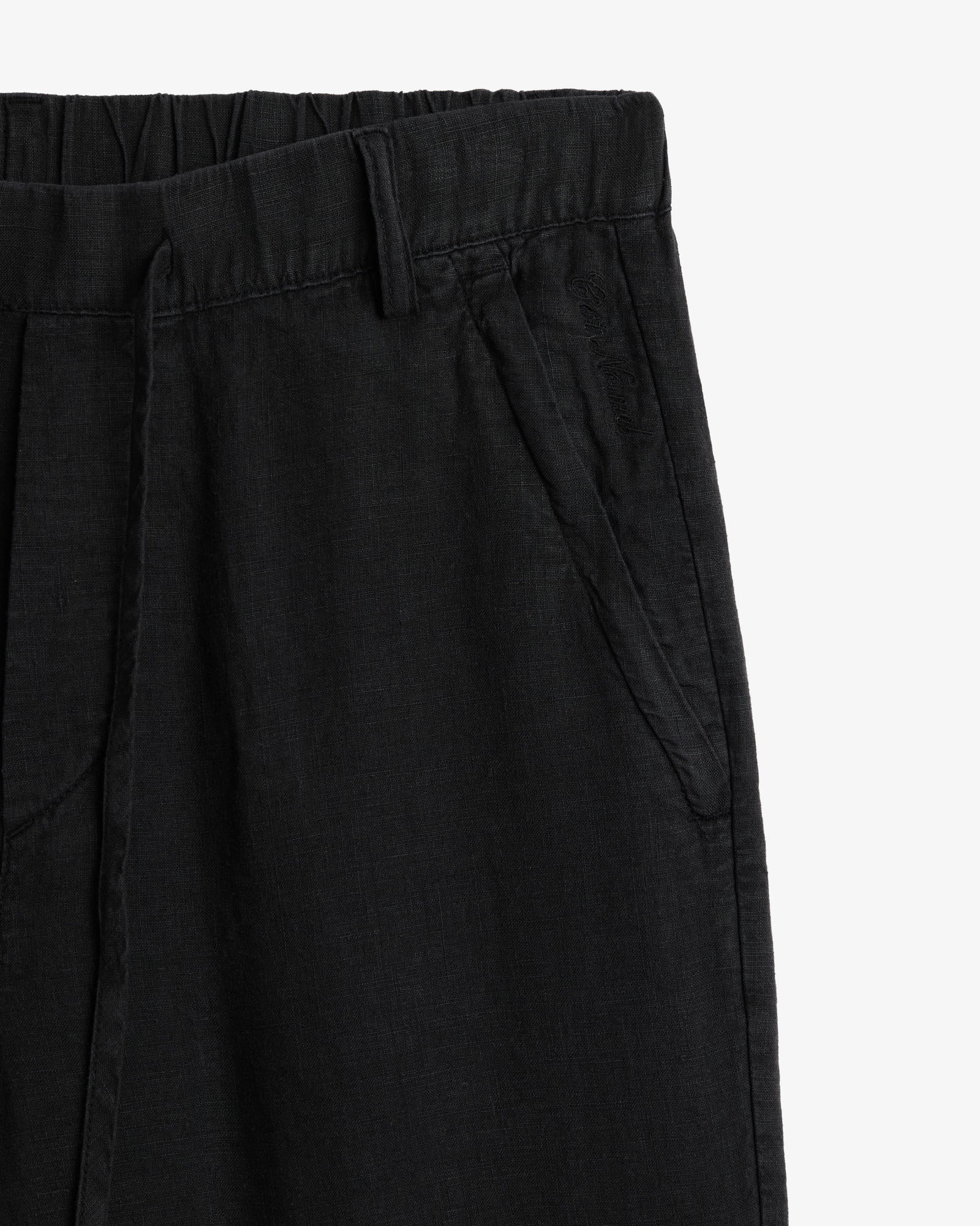 The Holiday Linen Trouser in black — close-up of the waistband and tonal C'est normal embroidery