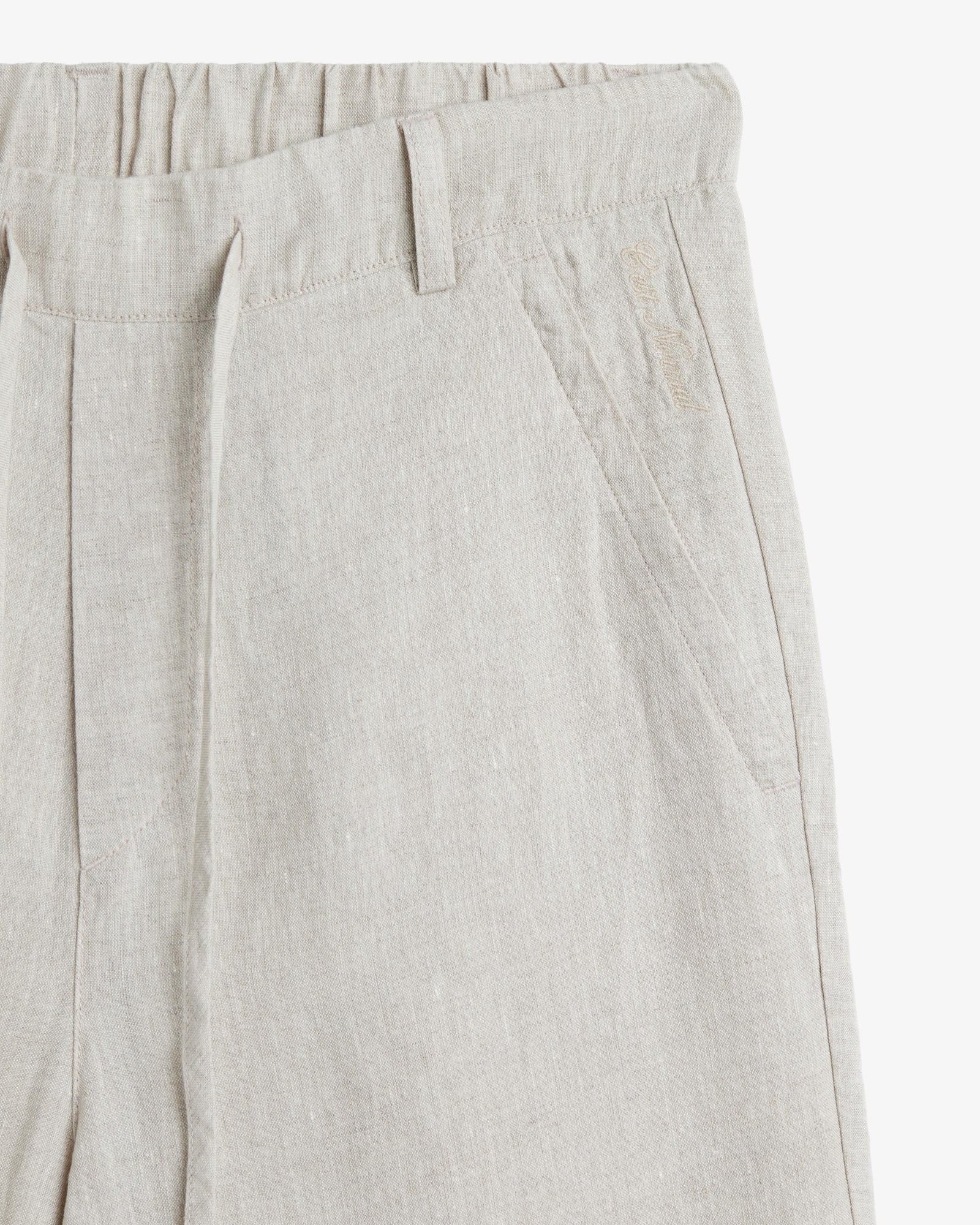 The Holiday Linen Trouser in natural — close-up of the waistband and embroidered logo