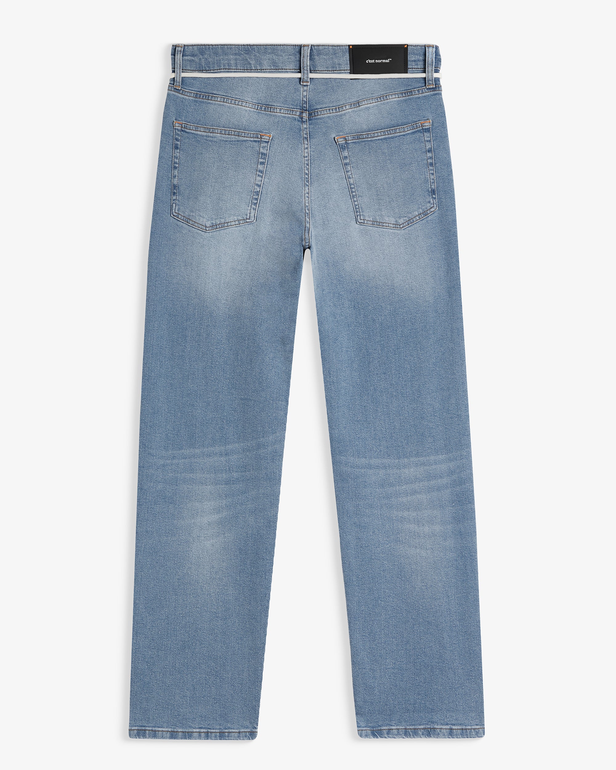 A back view of The Jeans Relaxed Straight Fit in Light Midwash, laid flat on a white background. The image highlights the two back pockets, the subtle orange accent stitching, and the rubber patch at the back waist with the c'est normal logo.