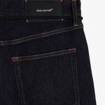 A close-up shot of the back of The Jeans Relaxed Straight Fit in Rinse Wash, laid flat on a white background. The image highlights the back pocket, subtle orange accent stitching, and the black rubber patch at the back waist featuring the c'est normal logo.