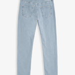 A back view of The Jeans Skinny Fit in light blue, laid flat on a white background. The image highlights the two back pockets, subtle orange accent stitching, and the black rubber patch at the back waist with the c'est normal logo.