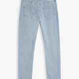 A back view of The Jeans Skinny Fit in light blue, laid flat on a white background. The image highlights the two back pockets, subtle orange accent stitching, and the black rubber patch at the back waist with the c'est normal logo.