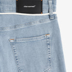 A close-up shot of the back of The Jeans Skinny Fit in Light Blue. The image highlights the black rubber patch with the c'est normal logo at the back waist, subtle orange accent stitching, and the back pocket details.