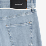 A close-up shot of the back of The Jeans Skinny Fit in Light Blue. The image highlights the black rubber patch with the c'est normal logo at the back waist, subtle orange accent stitching, and the back pocket details.