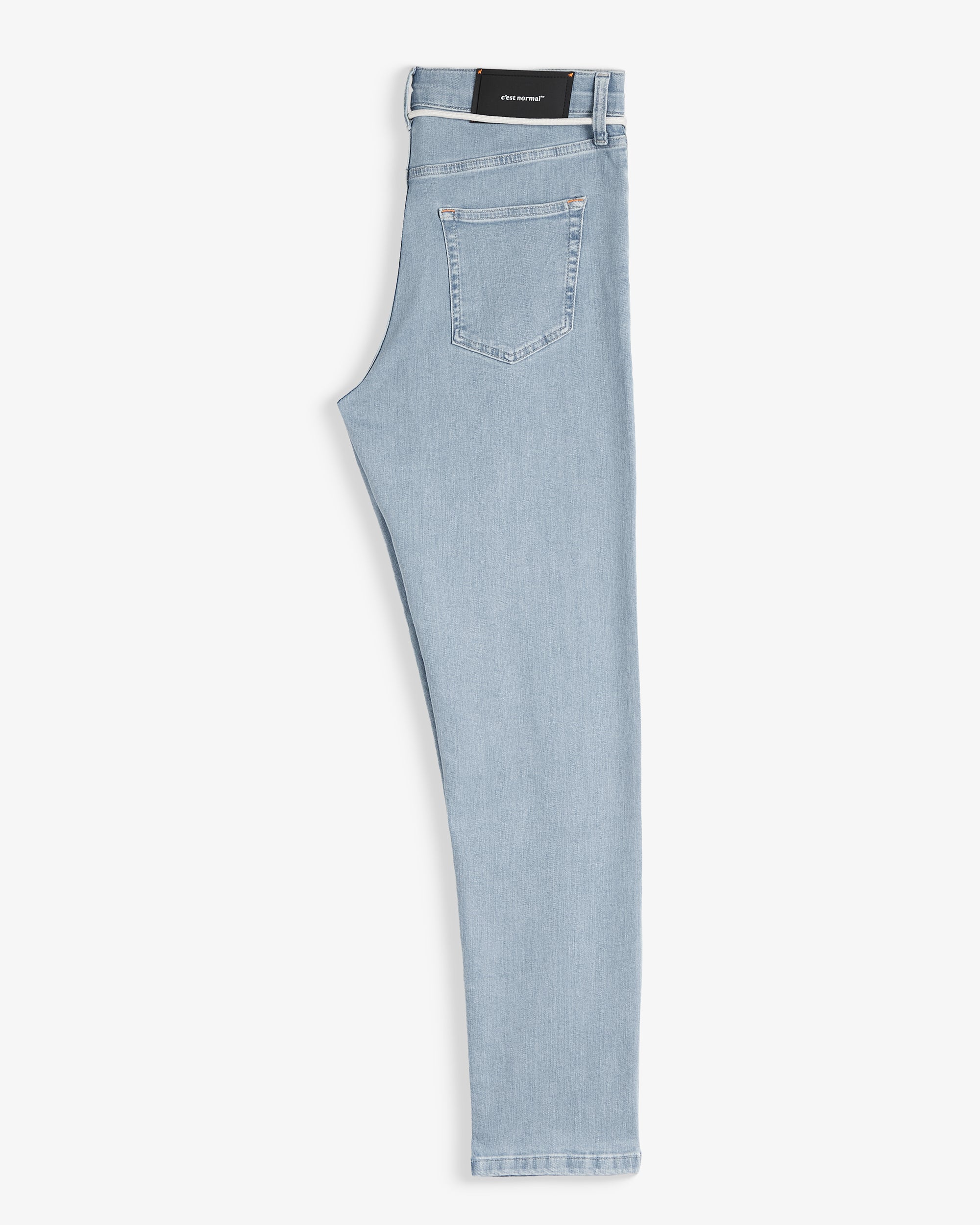 The Jeans Skinny Fit in light blue folded in half, laid flat on a white background, revealing the back pocket and the black rubber patch at the back waist with the c'est normal logo.
