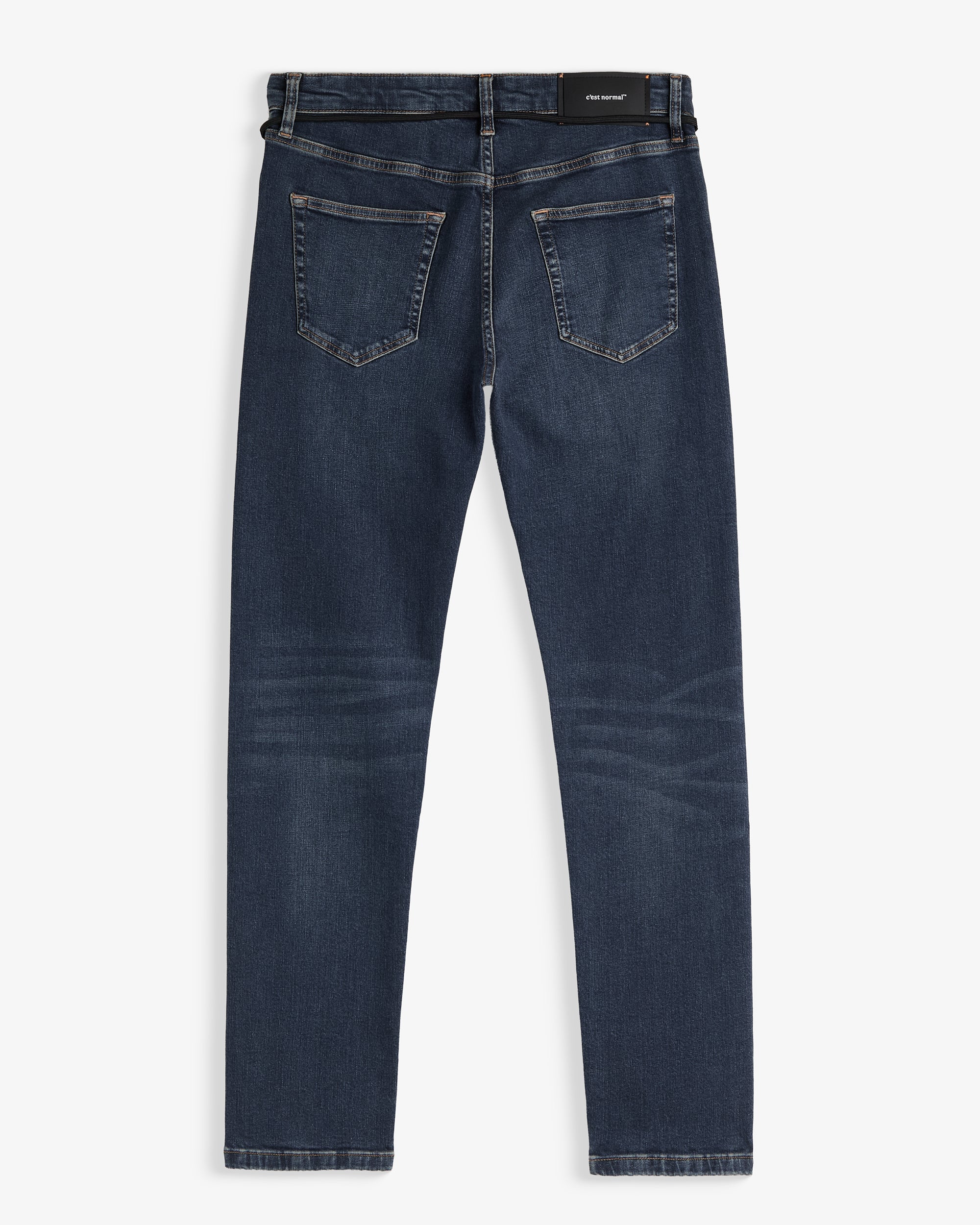 A back view of The Jeans Skinny Fit in Midwash, laid flat on a white background. The image highlights the two back pockets and the black rubber patch with the c'est normal logo at the waist.