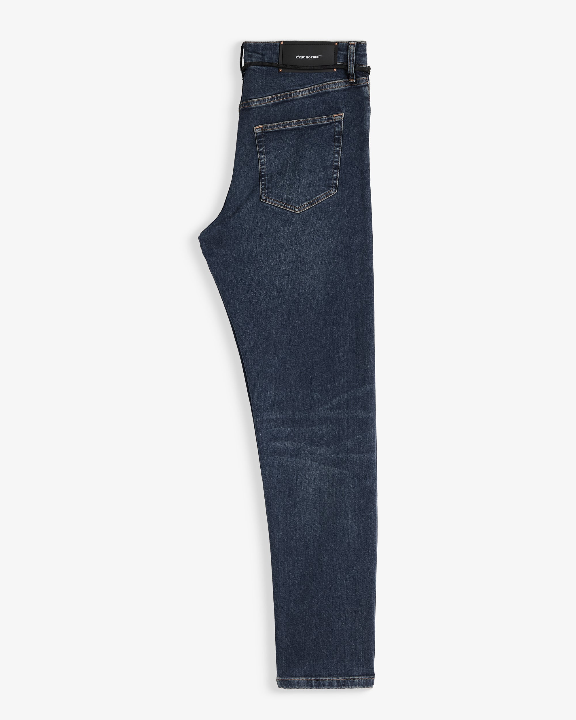 The Jeans Skinny Fit in Midwash folded in half and laid flat on a white background, highlighting the back pocket and the black rubber patch with the c'est normal logo on the waist.