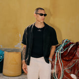 The Ribbed Tank Top in black — worn under an open black shirt next to fishing nets