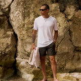 The Sanremo Linen Tee in white — worn with dark shorts and sunglasses against a rocky cliff