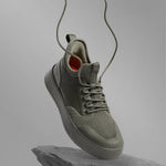 The Sneakers 2.0 in khaki — floating above a rock with laces flying in the air