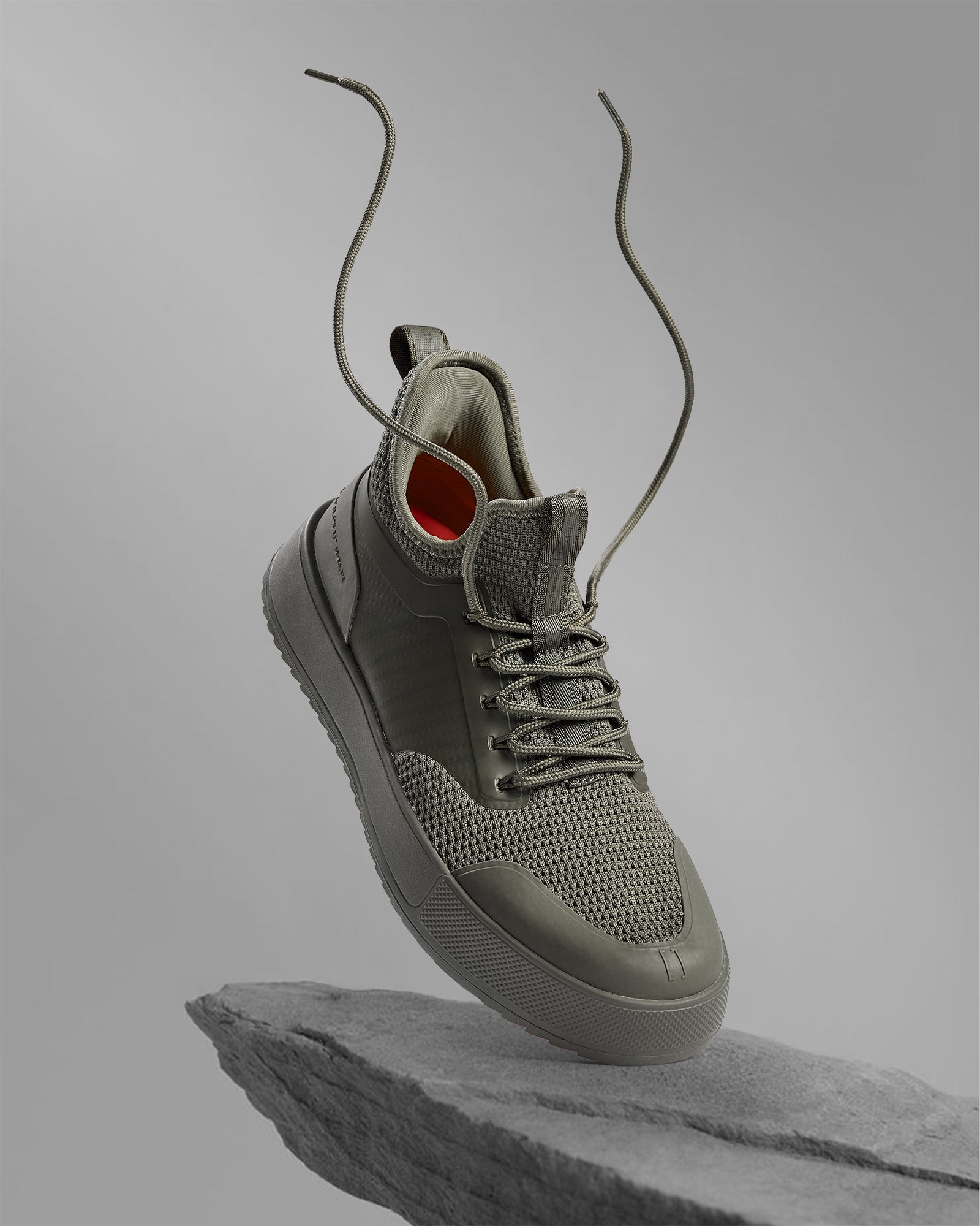 The Sneakers 2.0 in khaki — floating above a rock with laces flying in the air