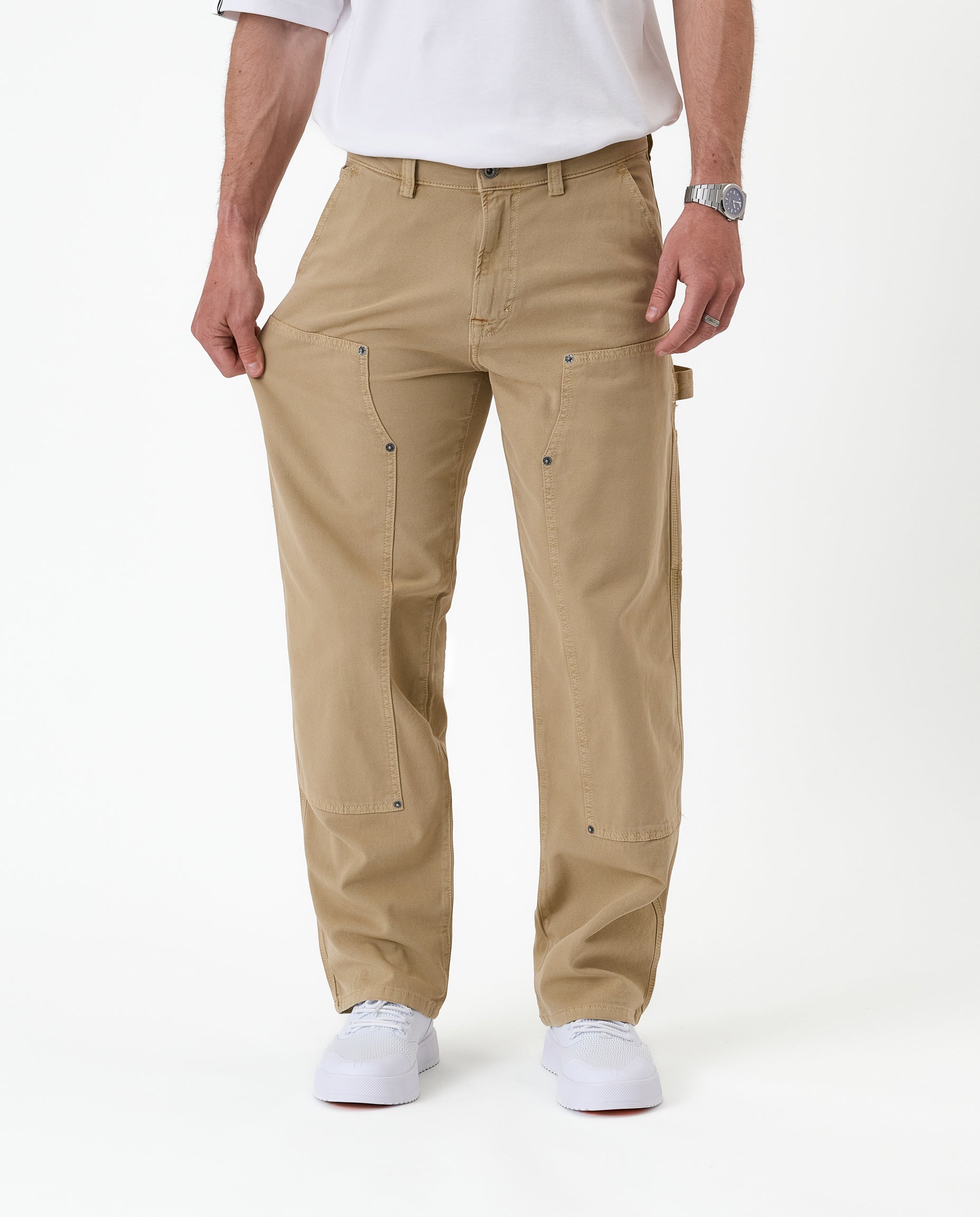 The Carpenter Pant in beige — showing the stretch fabric by pulling the leg