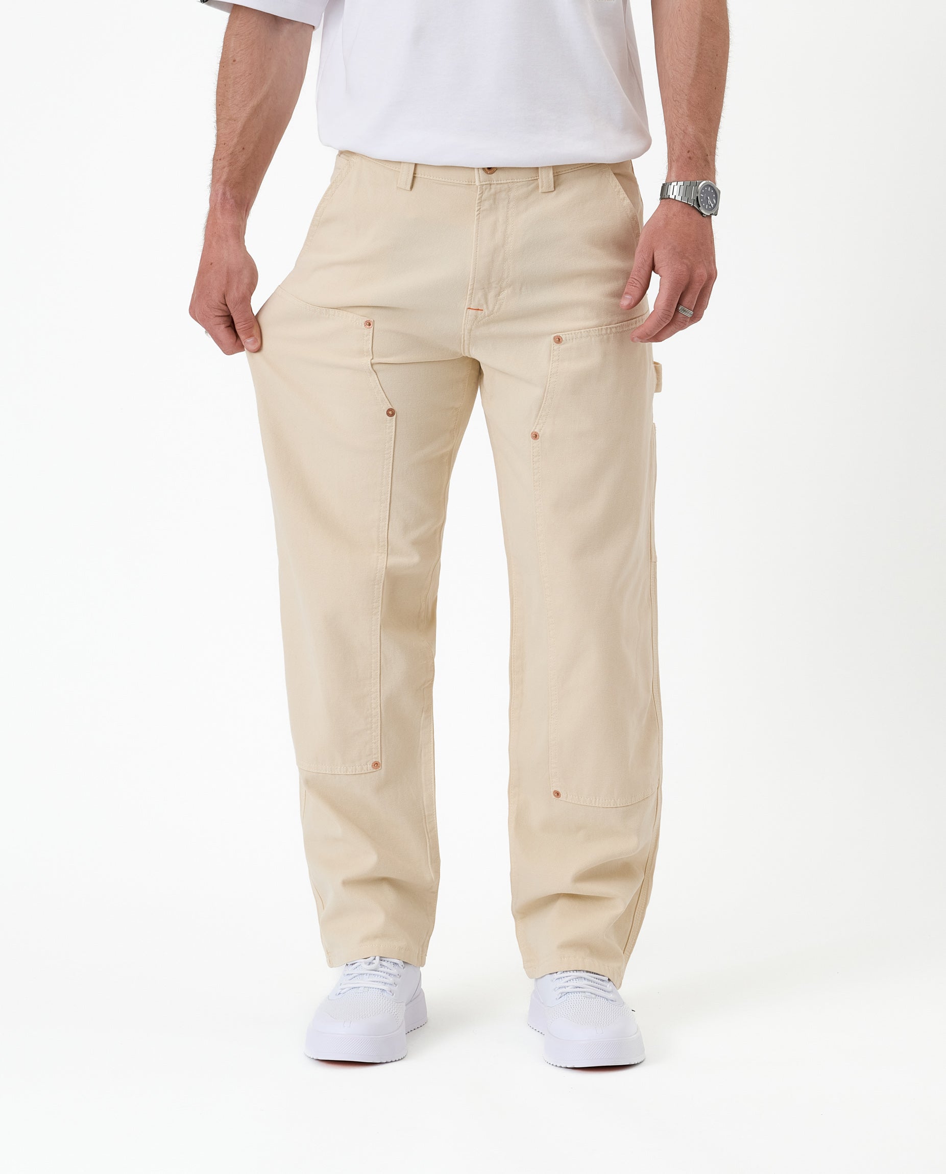 The Carpenter Pant in sand — pulled at the thigh to demonstrate the stretch fabric