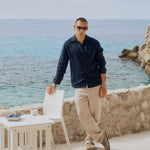 The Daily Linen Shirt in navy — worn with light trousers while standing by the sea