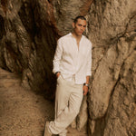 The Daily Linen Shirt in off-white — leaning against a rocky cliff wall