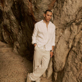 The Daily Linen Shirt in off-white — leaning against a rocky cliff wall