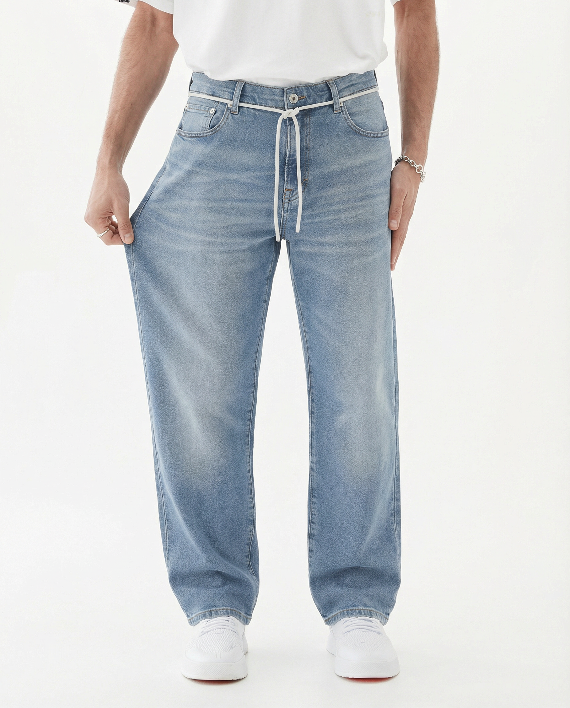 A front view of a model wearing The Jeans Relaxed Straight Fit in light midwash, standing against a white background. The model is pulling the fabric on the leg to demonstrate the stretch of the c'est normal jeans.