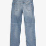 A back view of The Jeans Slim Fit in Light Midwash, laid flat on a white background. The image highlights the two back pockets and the black rubber patch at the back waist with the c'est normal logo.