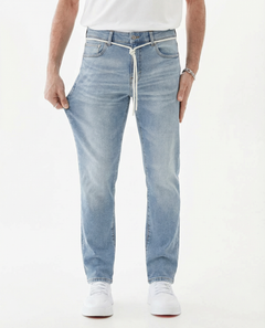 A model wearing The Jeans Slim Fit in Light Midwash and a white t-shirt, pulling on the side of the jeans to demonstrate the stretch of the Motion Fabric, set against a white background.