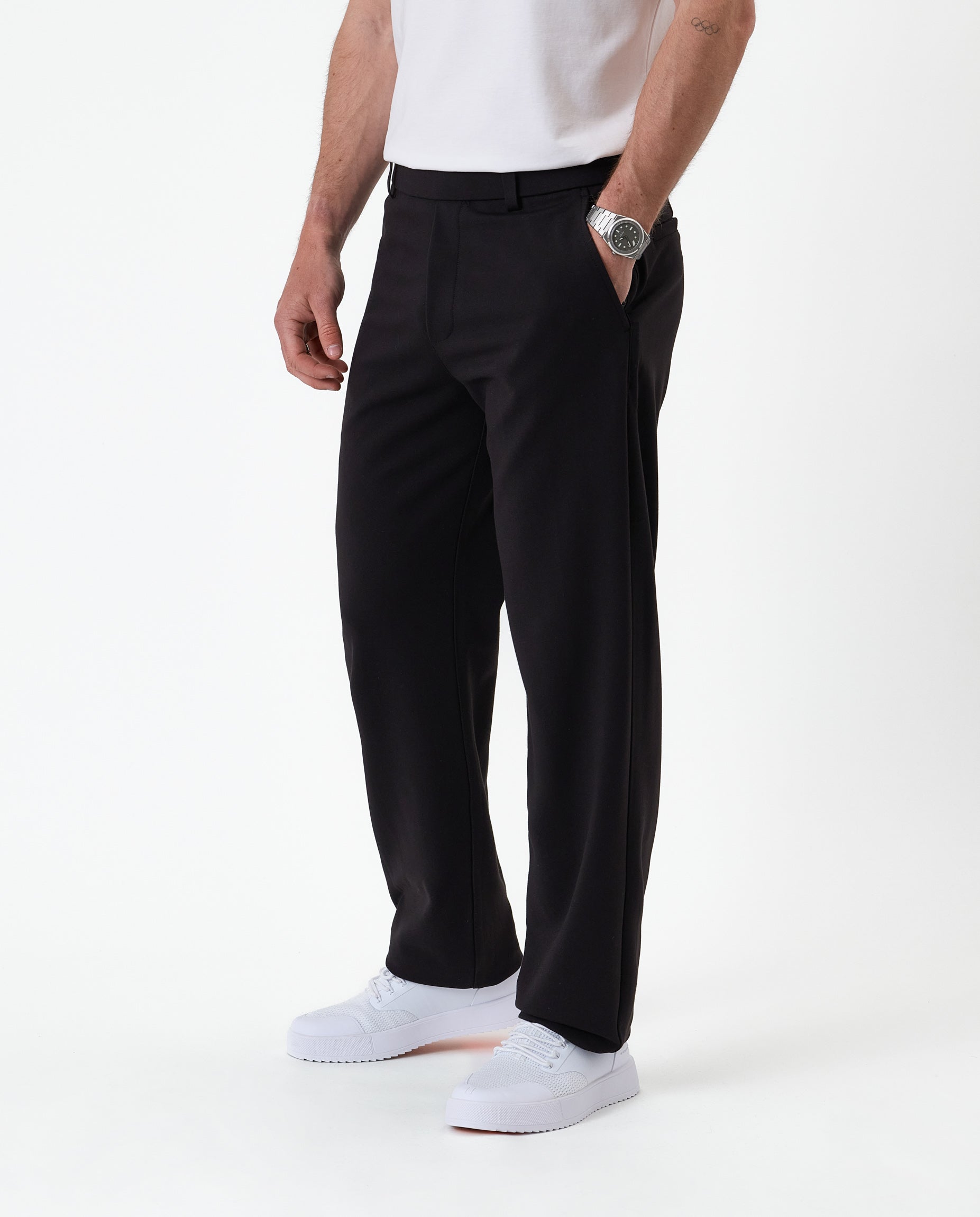 The Proper Pant Relaxed Straight Fit in black — side view styled with white sneakers