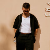 The Ribbed Tank Top in white — worn under an open black shirt with the C'est normal chest logo