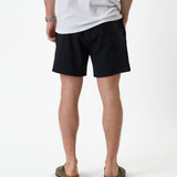The Shorts in black — back view worn with a white t-shirt and olive sandals