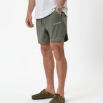 The Shorts in mulled green — side view showing the white logo and notched hem
