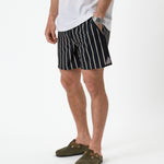 The Shorts in noir stripe — worn with a white t-shirt and olive green clogs