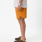 The Shorts in orange peel — side view showing the notched hem and black brand logo