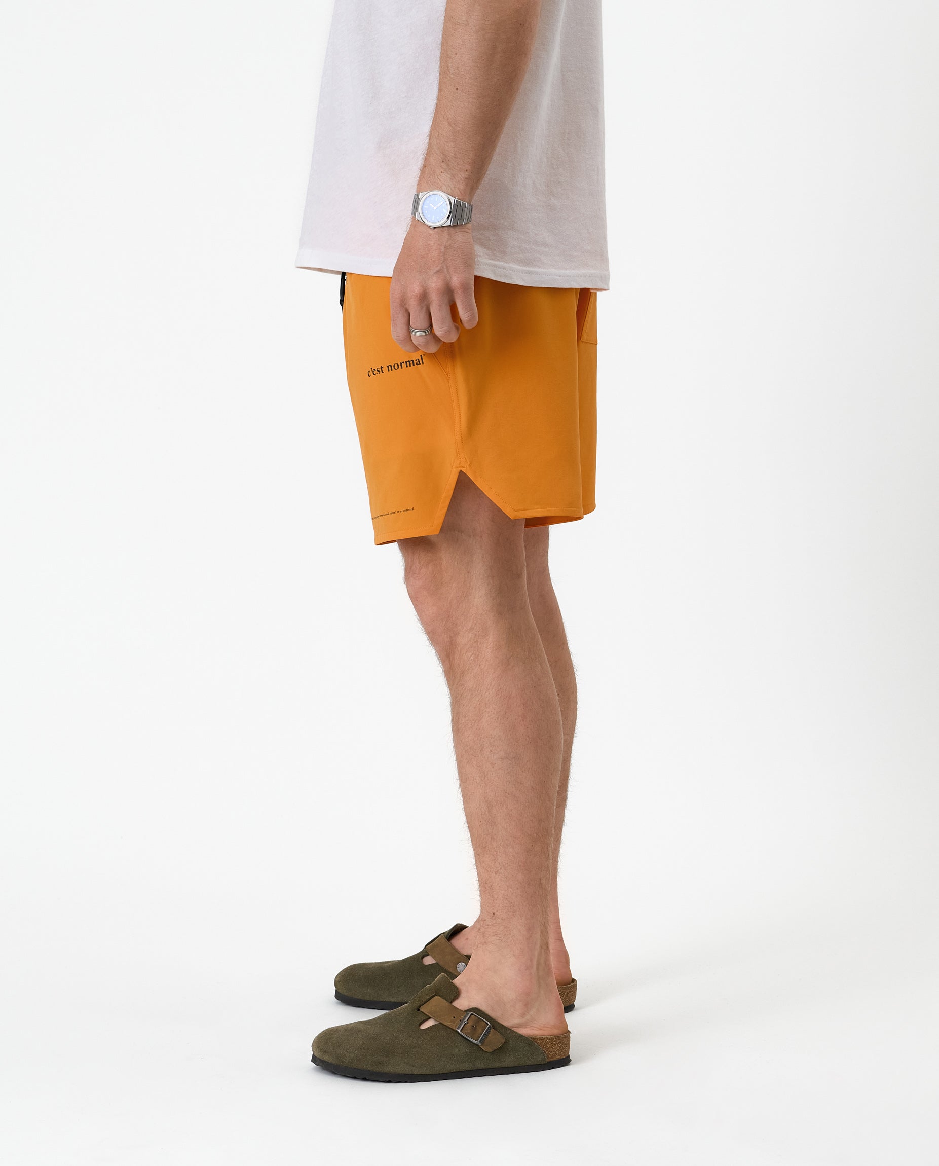 The Shorts in orange peel — side view showing the notched hem and black brand logo