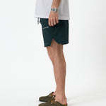 The Shorts in pine — side view showing the notched hem and white C'est normal logo