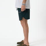The Shorts in pine — side view showing the notched hem and white C'est normal logo