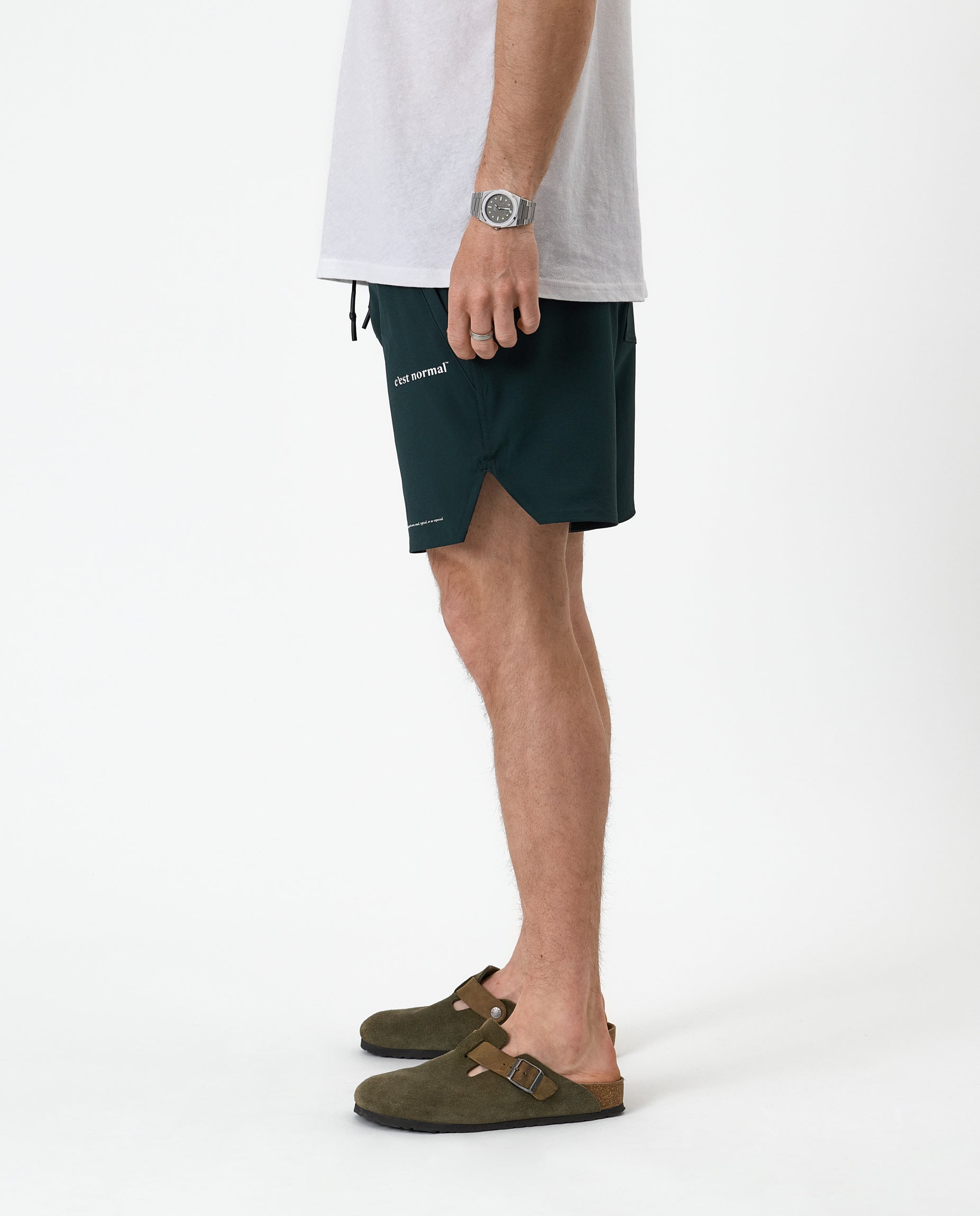 The Shorts in pine — side view showing the notched hem and white C'est normal logo
